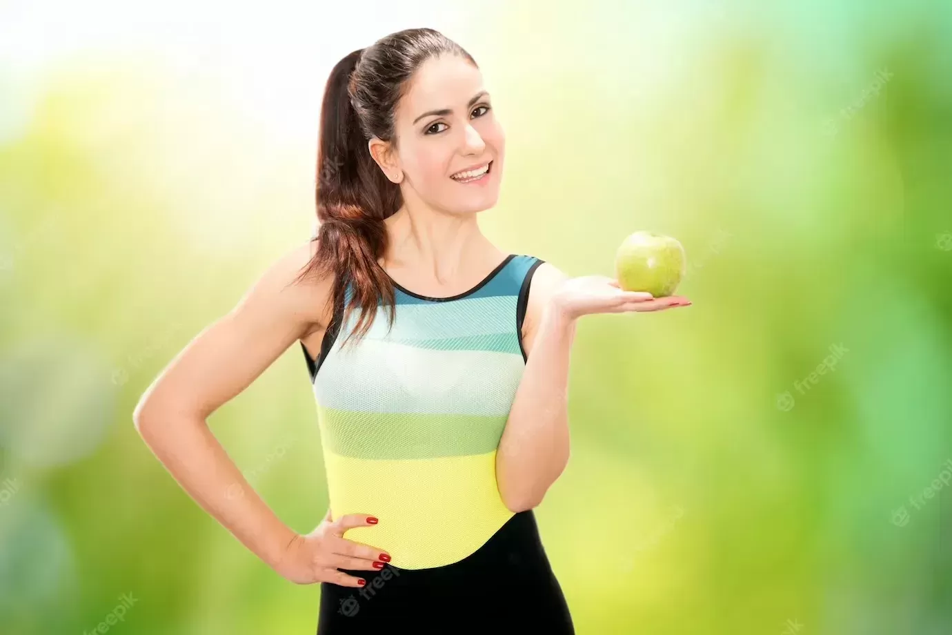 Portrait of happy smiling young beautiful woman in fitness wear with apple