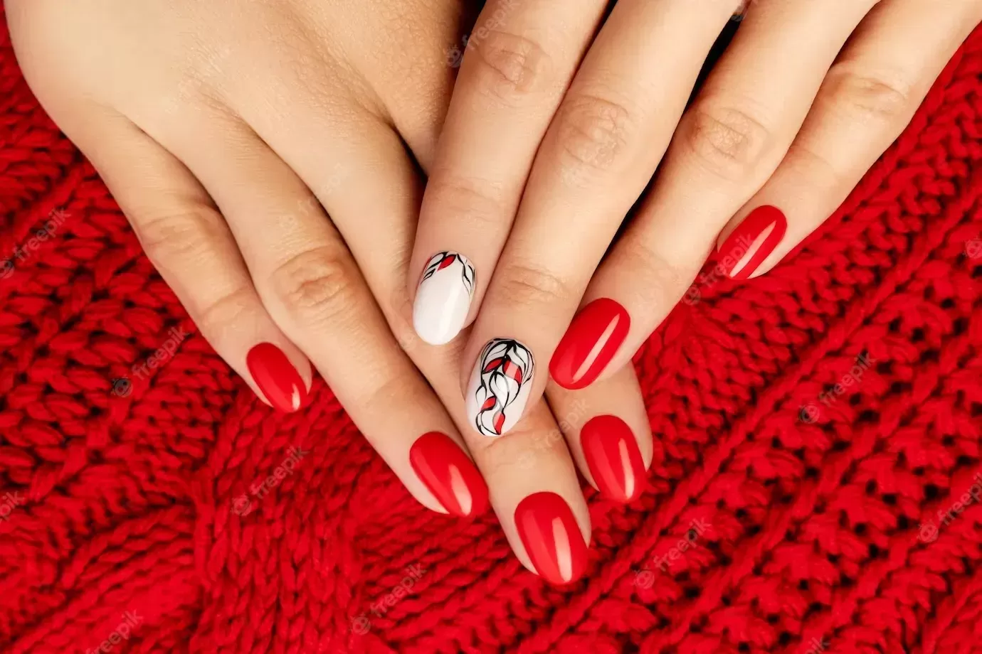 Woman’s hand in sweater with red manicure on gray