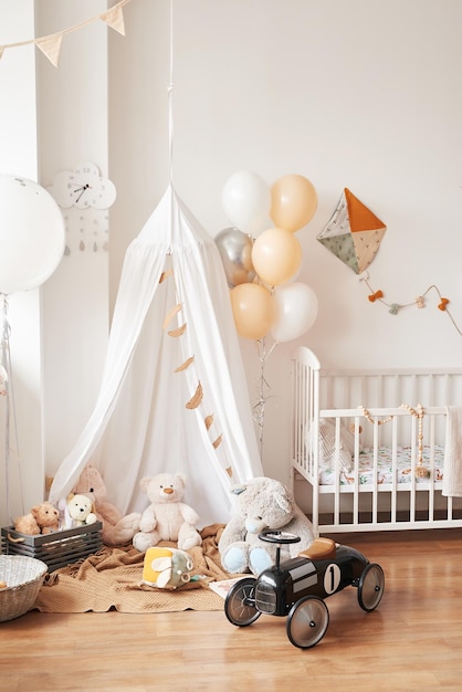 Scandinavian style white interior children’s room, bedroom, nursery. Baby cot with canopy. Wooden shelves and toys. Canopy tent, textile kite and balloons